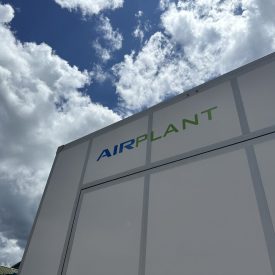 Low-angle view of a white rectangular structure with the text “AIRPLANT” against a cloudy blue sky.